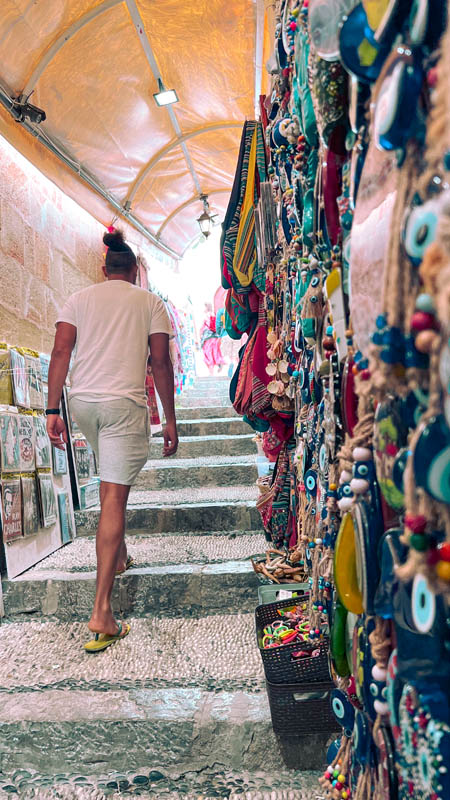 a man walking up steps next to a shop in lindos to the acropolis