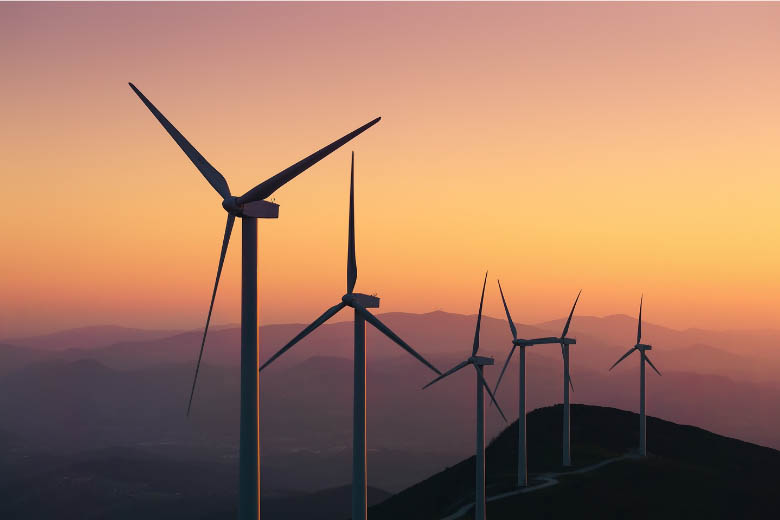 wind turbines generating renewable, green electricity in germany against a backdrop of a sunset with mountains in the background