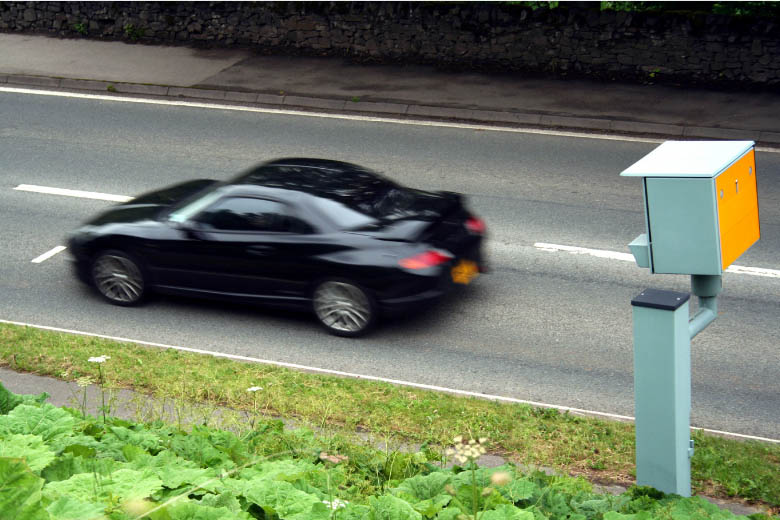a speeding camera pointed at a black car driving along a road