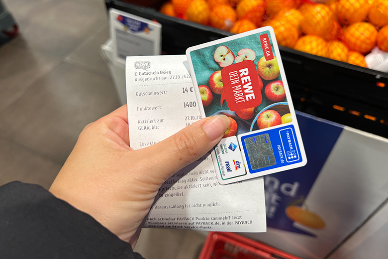 a person holding a cashback voucher and rewe payback card in a supermarket in germany