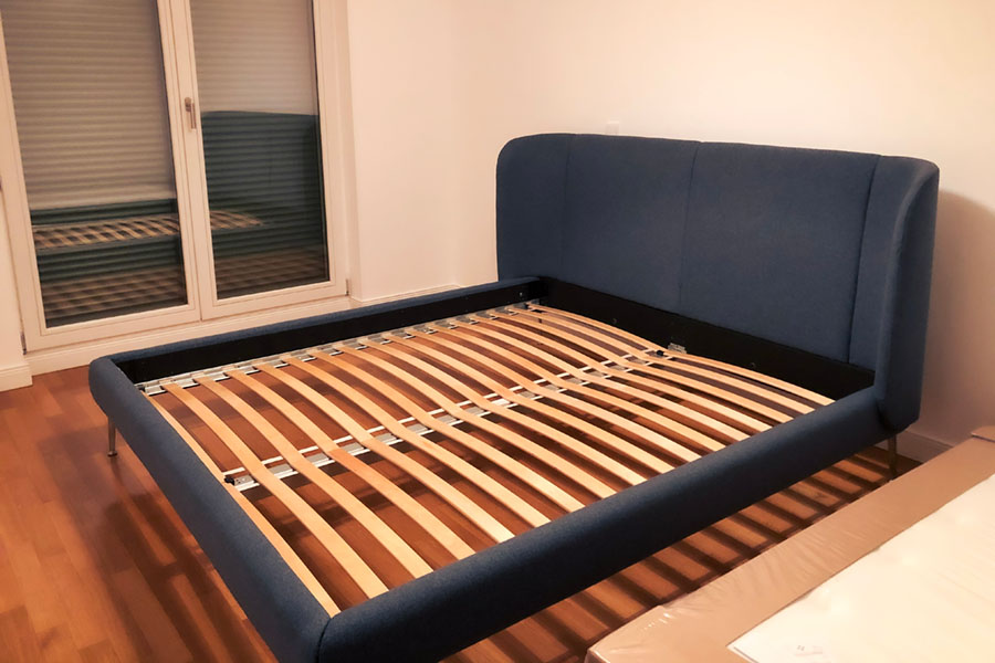 a modern blue upholstered bed frame with wooden slats, positioned in a bright interior bedroom near a window