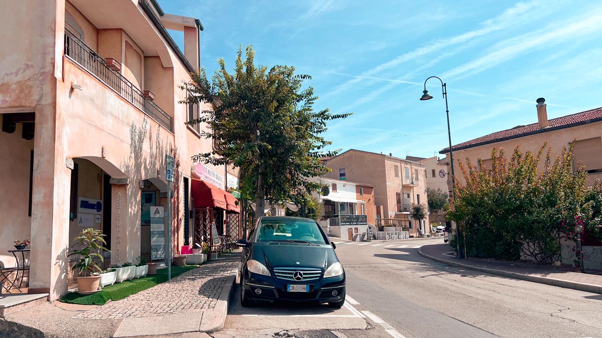 main road in the town of badesi sardinia with restaurants and cafes along the street and a black car parked in front