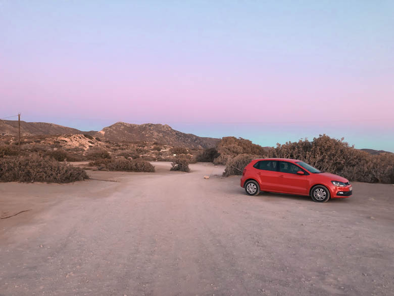 a red vw polo parked on a unpaved parking near elafonissi beach at sunset