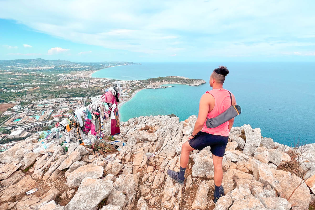 a man standing at the summit of the kolymbia rock hiking trail in rhodes greece with a view of the aegean sea