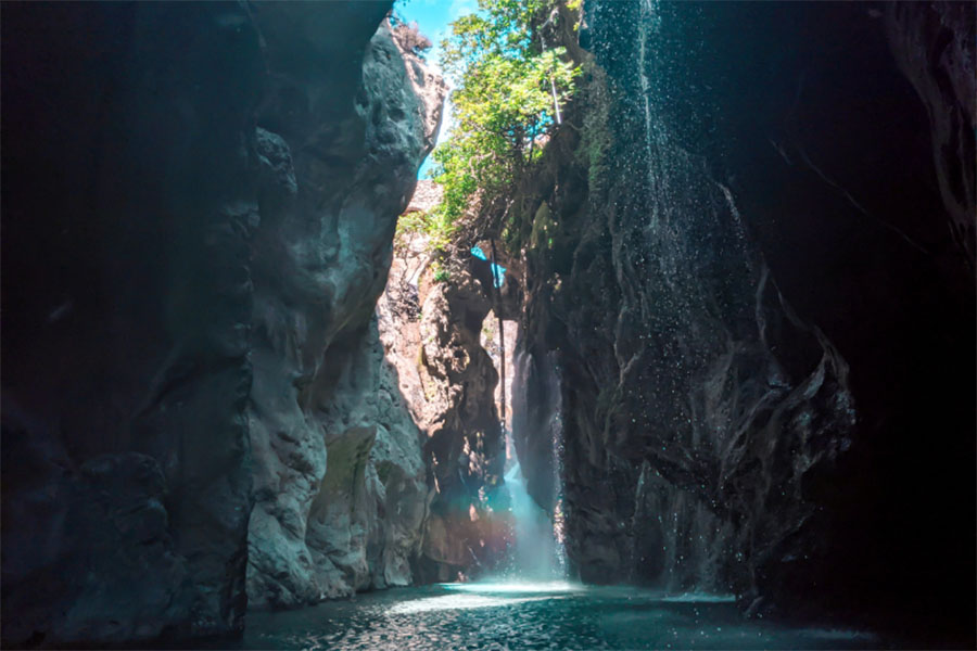 the cascades of waterfall in the deep gorge of Kourtaliotiko with trees on the side of the canyon