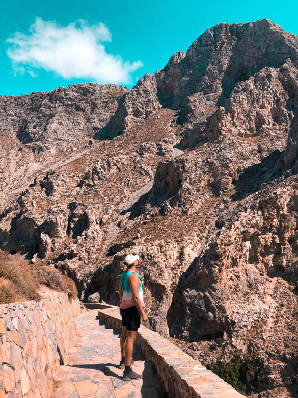 a man standing on paved stairs in greece looking up at rocky mountains