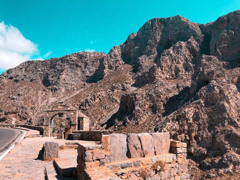 a stone arch alongisde the road in crete marking the entrance to the hiking trail that leads down to kourtaliotiko gorge waterfall