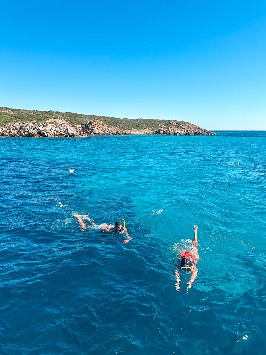 a man and a woman snorkeling in crystal clear electric blue waters off la maddalena island in north sardinia
