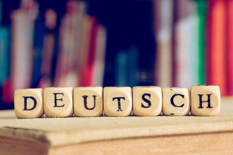 a close-up of dice placed next to each other to spell the word Deutsch placed in front of a row of books in the background