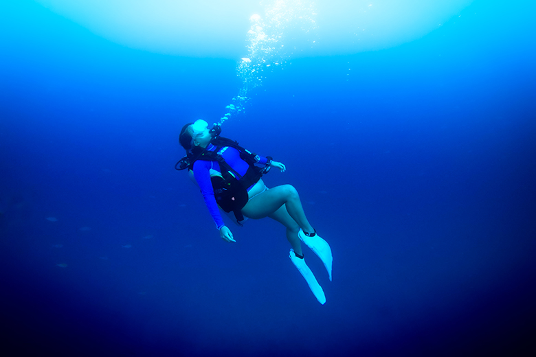a woman scuba diving in the deep blue ocean wearing a rash guard, BCD, air tank and diving fins