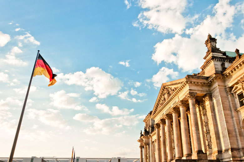 a German flag affixed to a pole flying in the air in front of the Deutscher Bundestag parliament building in Berlin