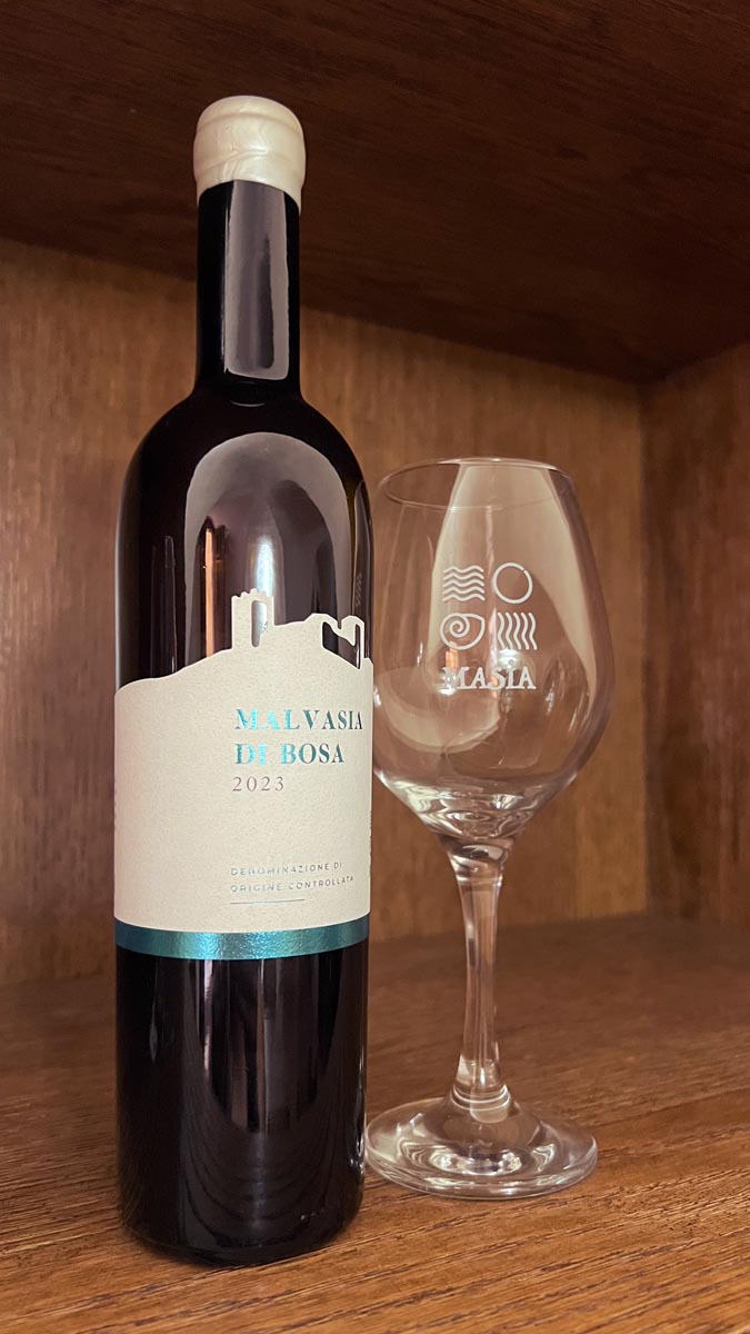 a bottle of malvasia di vosa wine next to a wine glass taken at a winery in bosa