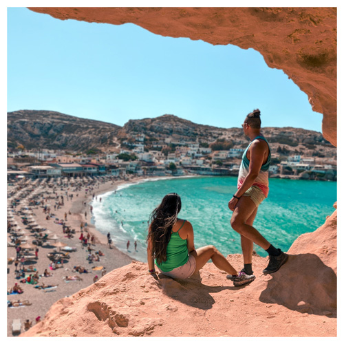 a couple standing inside the Matala caves looking over and admiring the views of Matala Beach in the distance