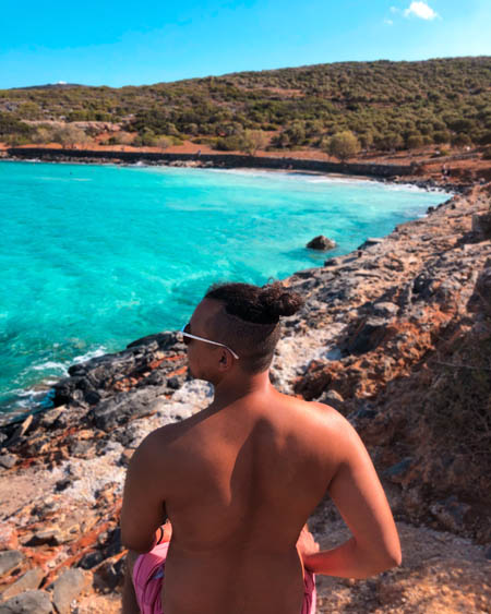 candid instagram photography of a man sitting on a rock overlooking a beautiful beach in crete