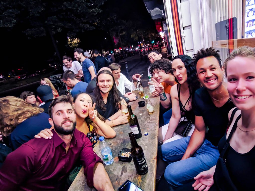 group of expats sitting around a wooden table outside a late shop or späti in berlin