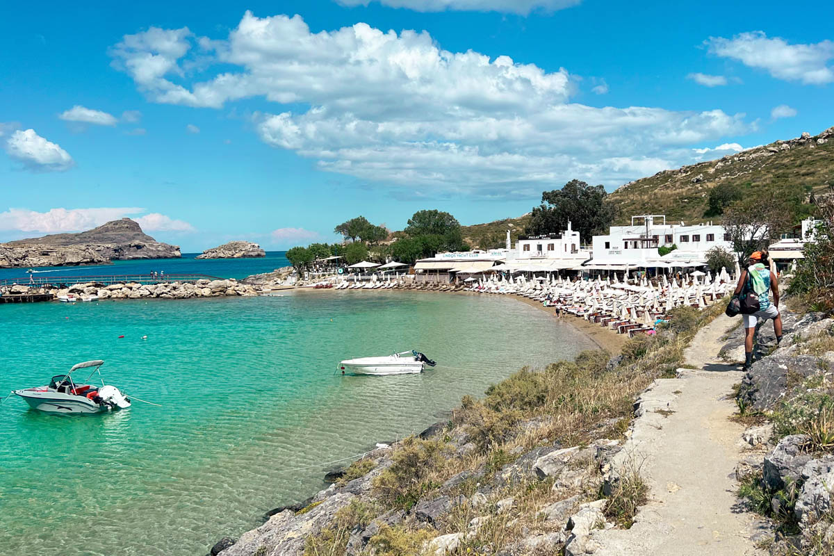 a tiny beach in lindos rhodes with a white restaurant and sunbeds on the white sand