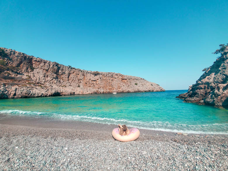 a woman sitting in a donut float on beautiful, off the beaten track pebble beach in crete greece called paralia menies beach