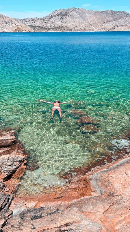 a man floating in crystal clear water at plaka beach simi island greece