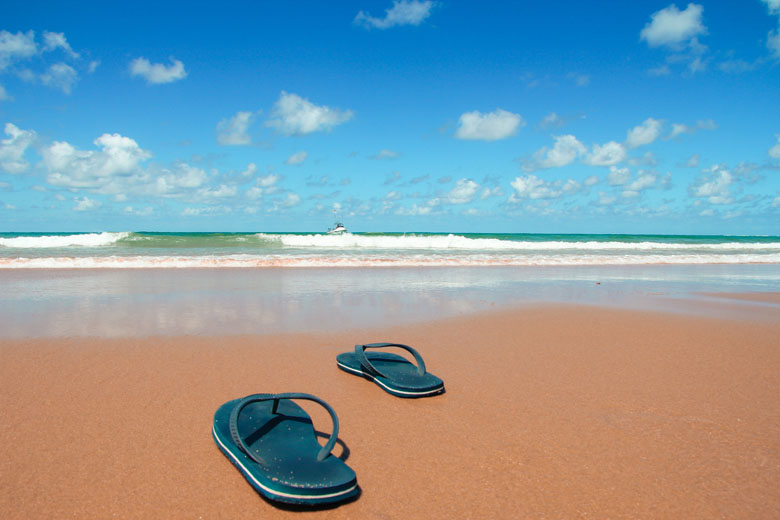 a pair of navy flip flops on Ponta do Ouro beach and a fishing boat approaching the shore in the distance