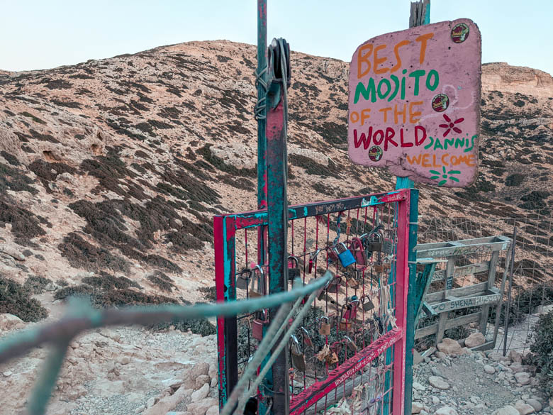 a pink sign that says best mojito of the world on the red beach hiking trail from matala to nudist red beach
