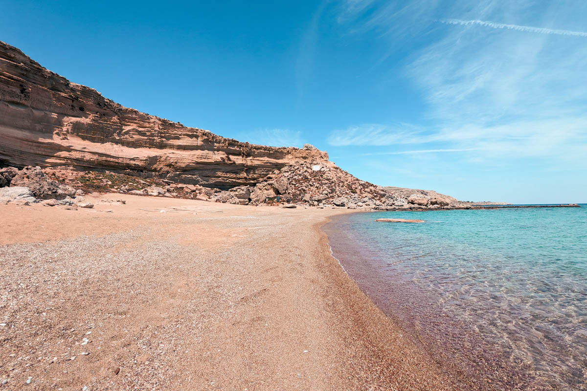 a view red sand beach with crystal clear turquoise water and limestone cliffs in the background