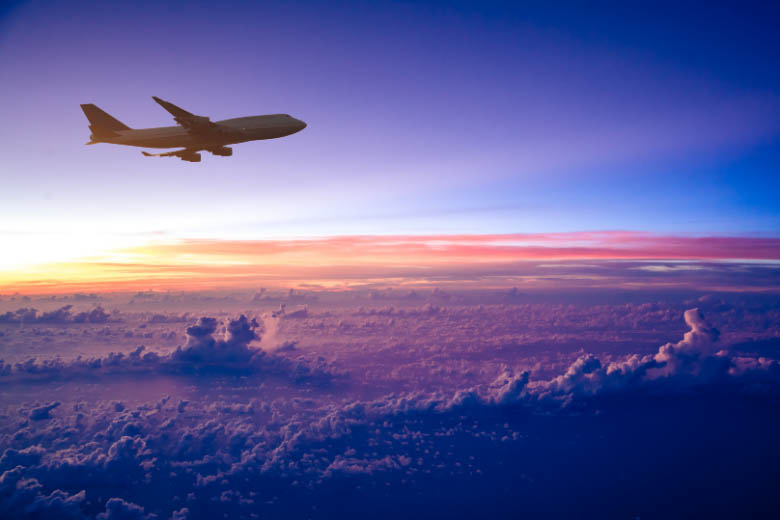 airplane flying above the clouds against a purple sky at sunset