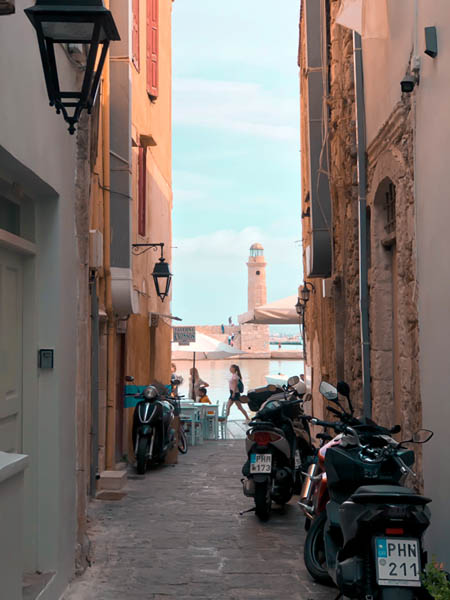 a view of the venetian harbor in old town rethymno photographed through a narrow alleyway with motorbikes on the side