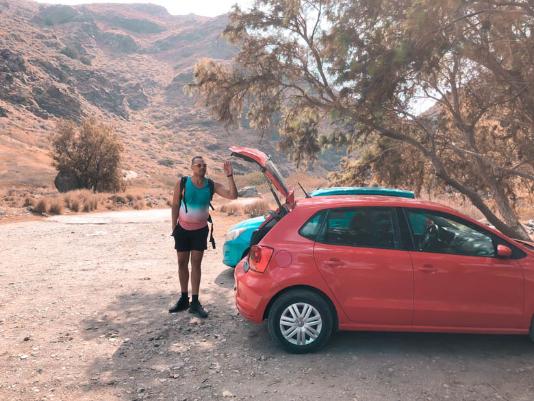 a man standing next to a car rental in an unpaved parking area near richtis gorge in crete