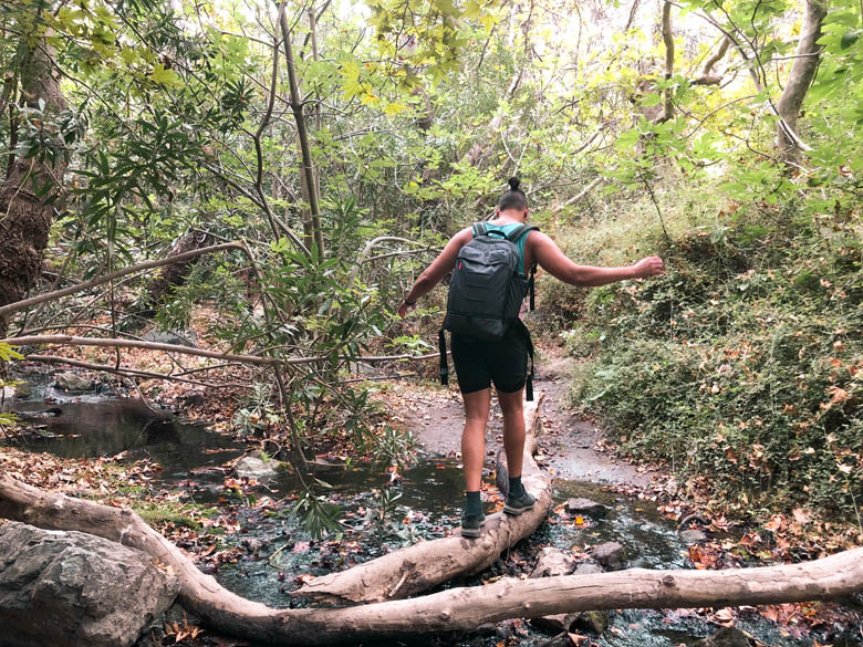 a man walking on a log to cross a stream in crete greece