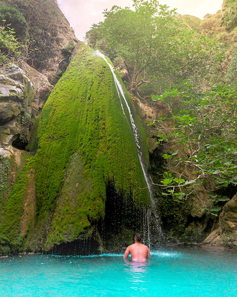 a man sitting in turquoise blue waters at the bottom of richtis gorge waterfall