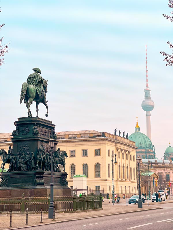 a historical monument with a man sitting on a horse in the city centre of berlin with the tv tower and berlin cathedral in the backdrop 