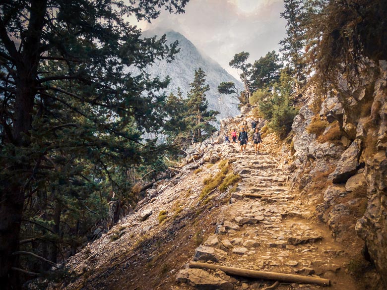 hikers walking down a steep path in crete with a view of the white mountains in the background