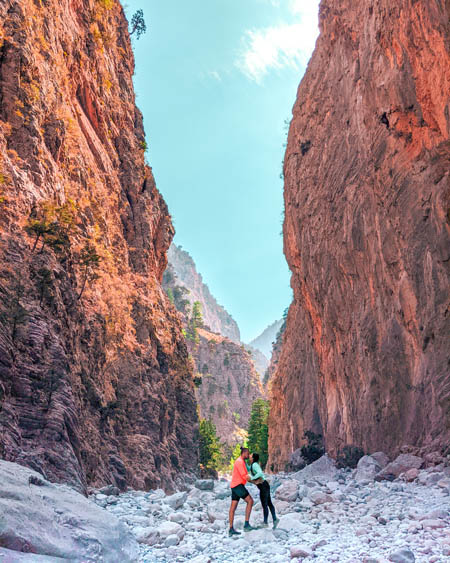 an instagrammable picture of a couple standing on white limestone rocks at the bottom of Samaria Gorge near the famous iron gates 