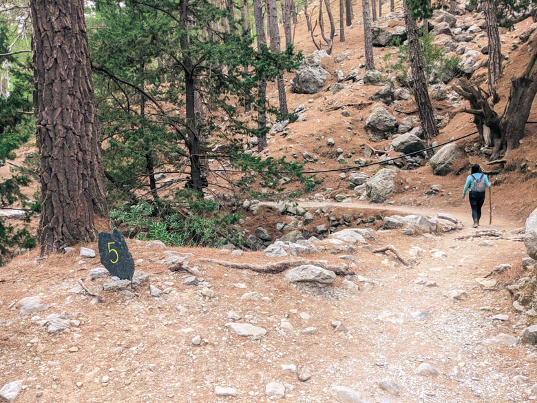 a woman hiking in crete with a view of a sign that says 5 on it indicating distance hiked