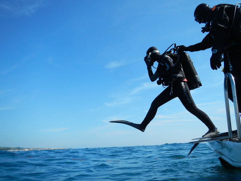 scuba diving dressed in full scuba dive gear entering the ocean using giant step technique