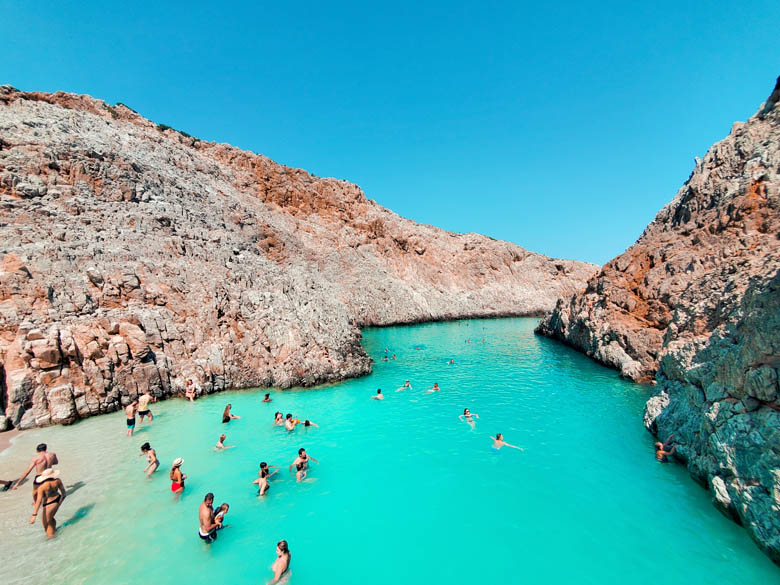 people swimming in the turquoise blue waters at seitan limania beach near chania on crete island, greece