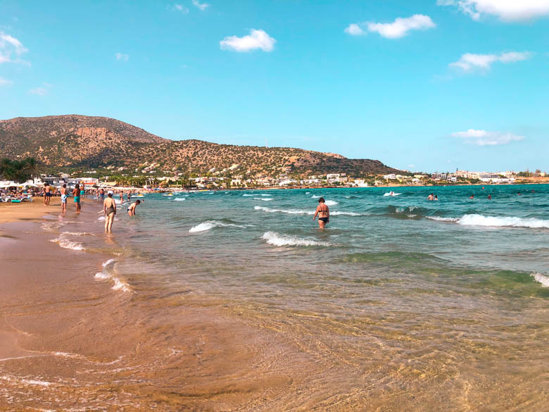 stalis beach at the resort town stalida with people swimming in the ocean and walking on the beach