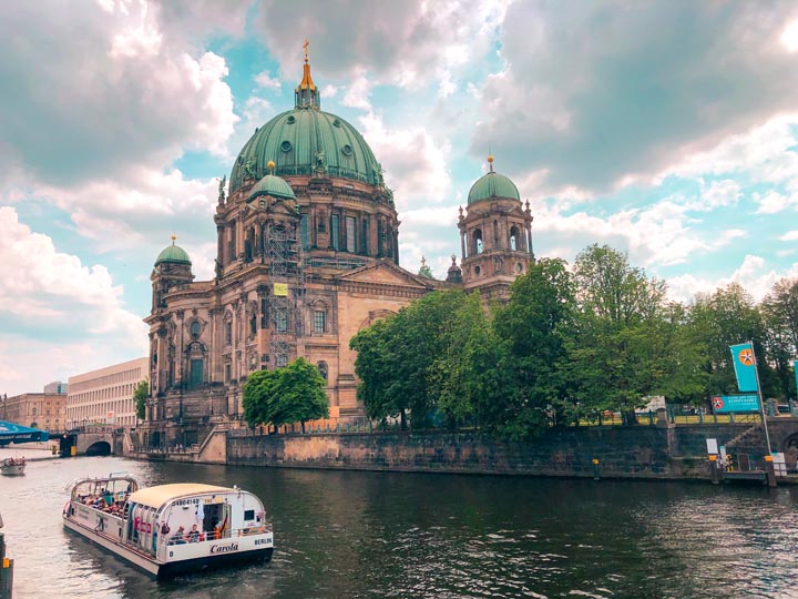 a view of the berlin cathedral in the city centre with a river cruise tour floating on the water
