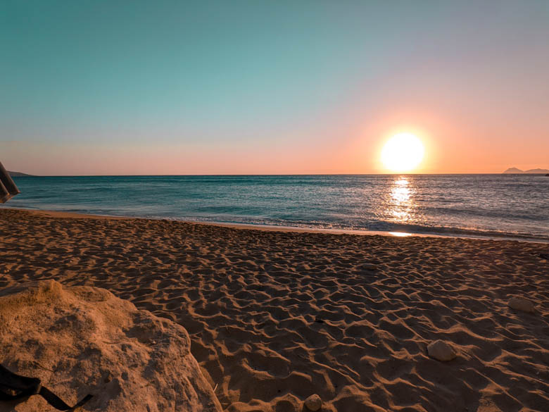 the best sunset spot at red beach with the orange sun setting in the horizon on the sandy beach in crete