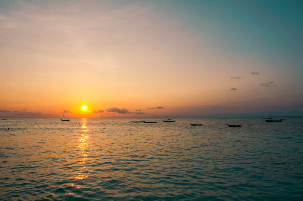 fiery orange sunset on the horizon at nungwi zanzibar beach with wooden traditional dhow boats floating on the surface