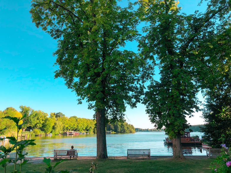 a woman sits on a bench with trees lining the edge of flakensee lake 