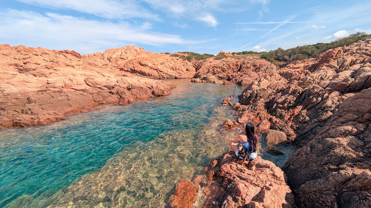 a woman and a dog sit on the rocks along the sentiero della torre nature trail in the town isola rossa in north central sardinia italy