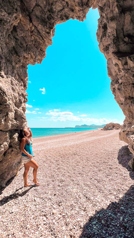 a woman standing inside traganou caves on a pebble beach