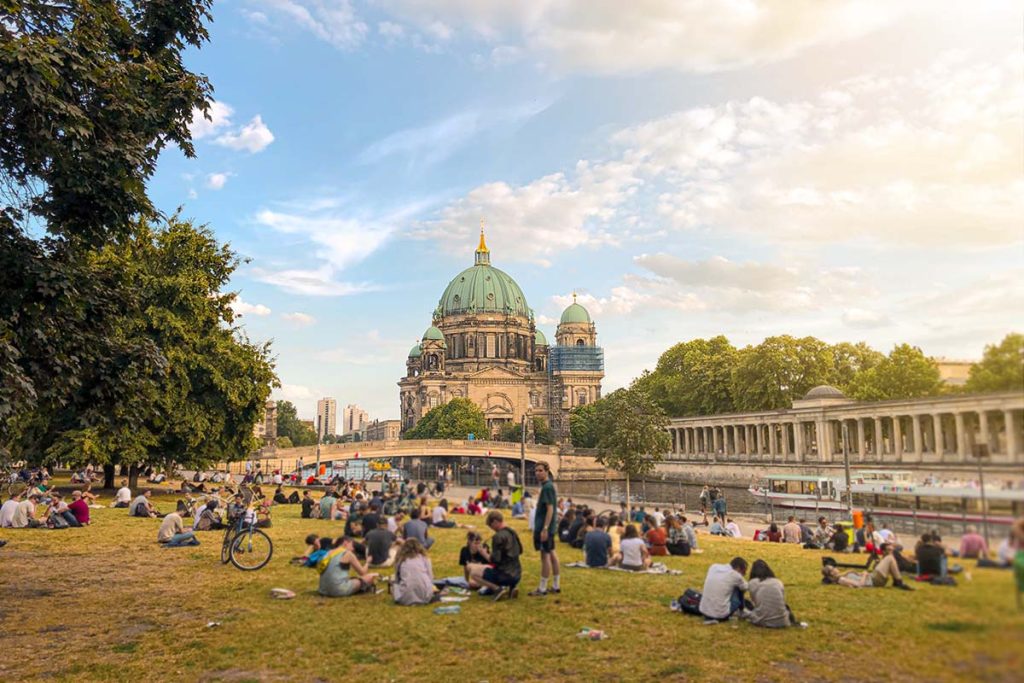 locals and tourists sitting on the grass in front of the berlin cathedral and museum island in germany