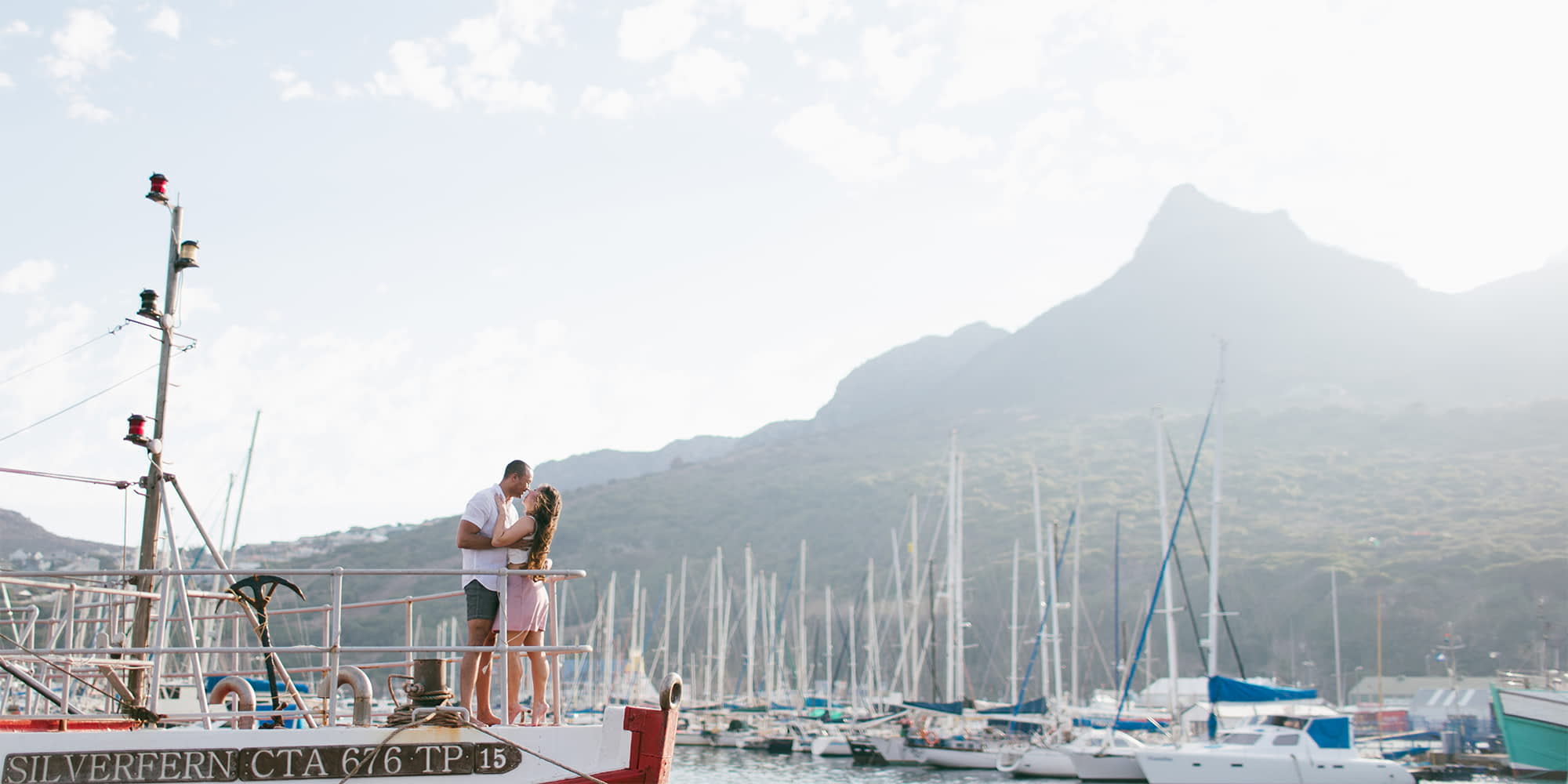 Michael and Chloe from Nomad And In Love embracing on the bow of ship which is docked in Hout Bay in Cape Town