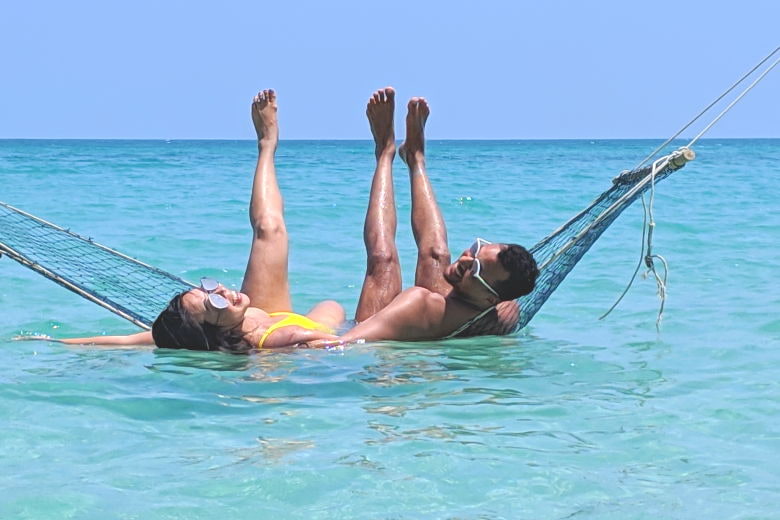a couple enjoying their cheap travel while sitting in a hammock that is suspended over the water at Bottle Beach in Thailand
