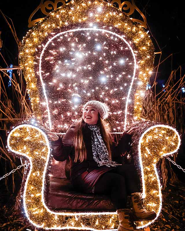 a woman smiling while seated on an armchair made of wire and decorated with dozens of brightly lit ferry lights