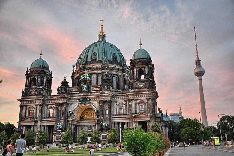 berliner dom in berlin germany with tv tower in the background and people on the front lawn abiding to social distancing measures during coronavirus pandemic