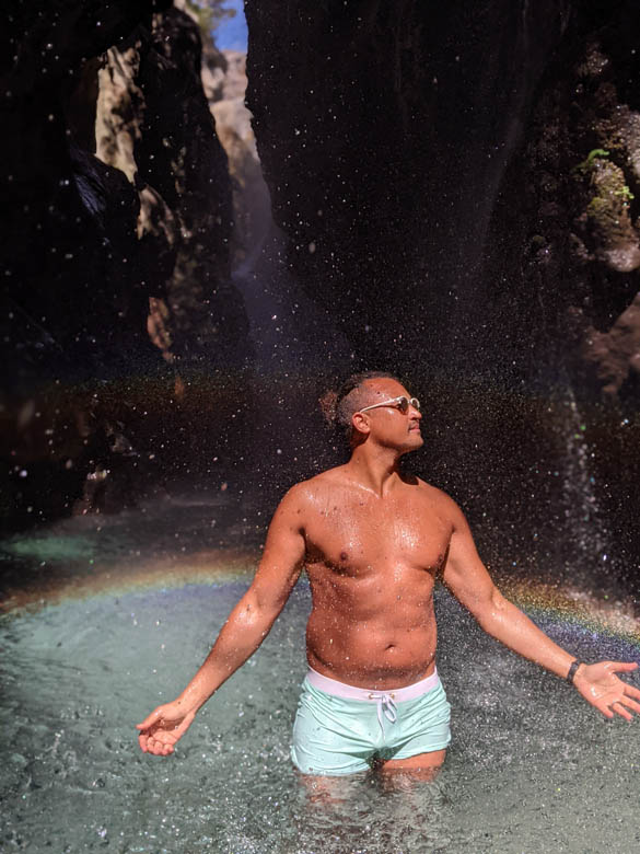 a man standing in knee deep crystal clears waters under waterfalls in crete