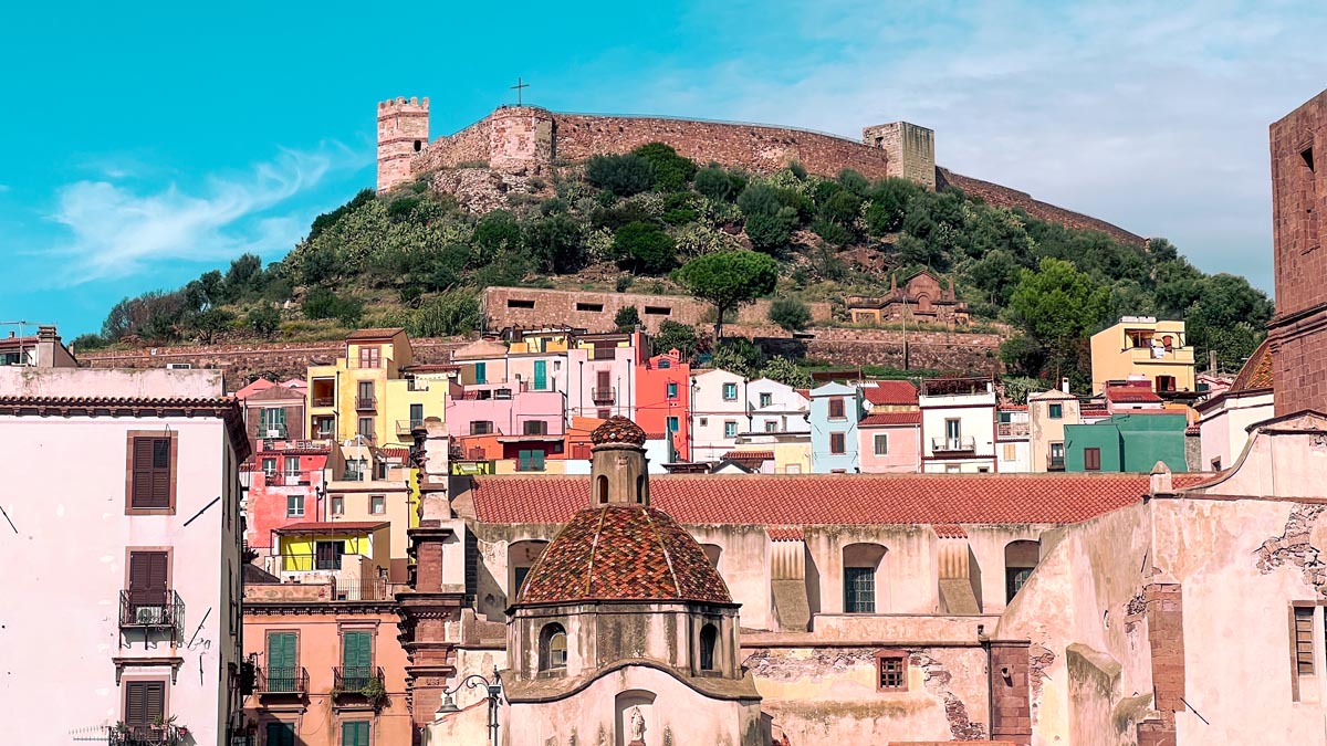 colourful houses and buildings packed together under a hill in bosa north west sardinia where the castle of serravalle sits on top